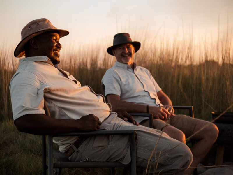 Two men sitting and smiling at sunset for a positive impact.