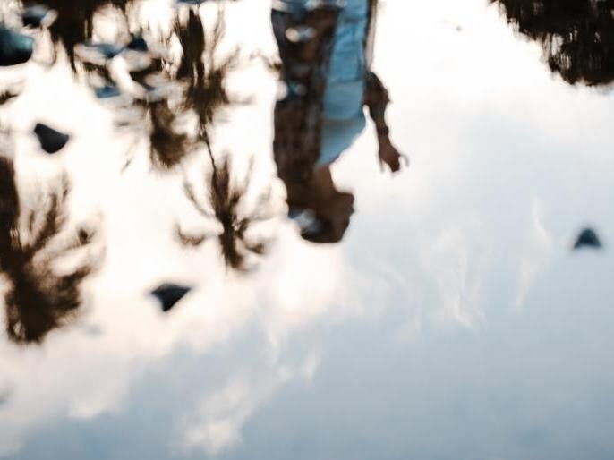 A reflection of a woman in the ocean with palm trees behind her