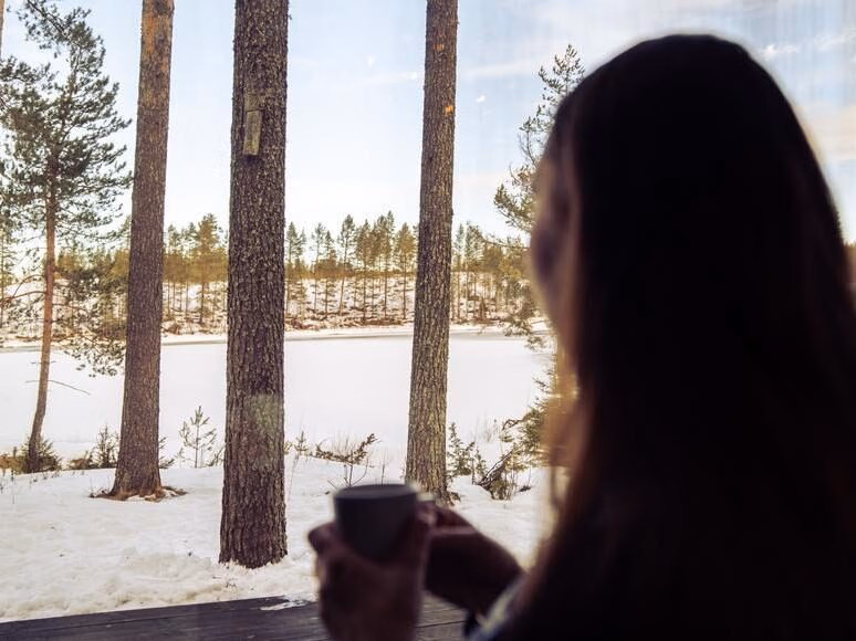 Woman looks out on snowy landscape in her luxury cabin in northern Sweden luxury trip