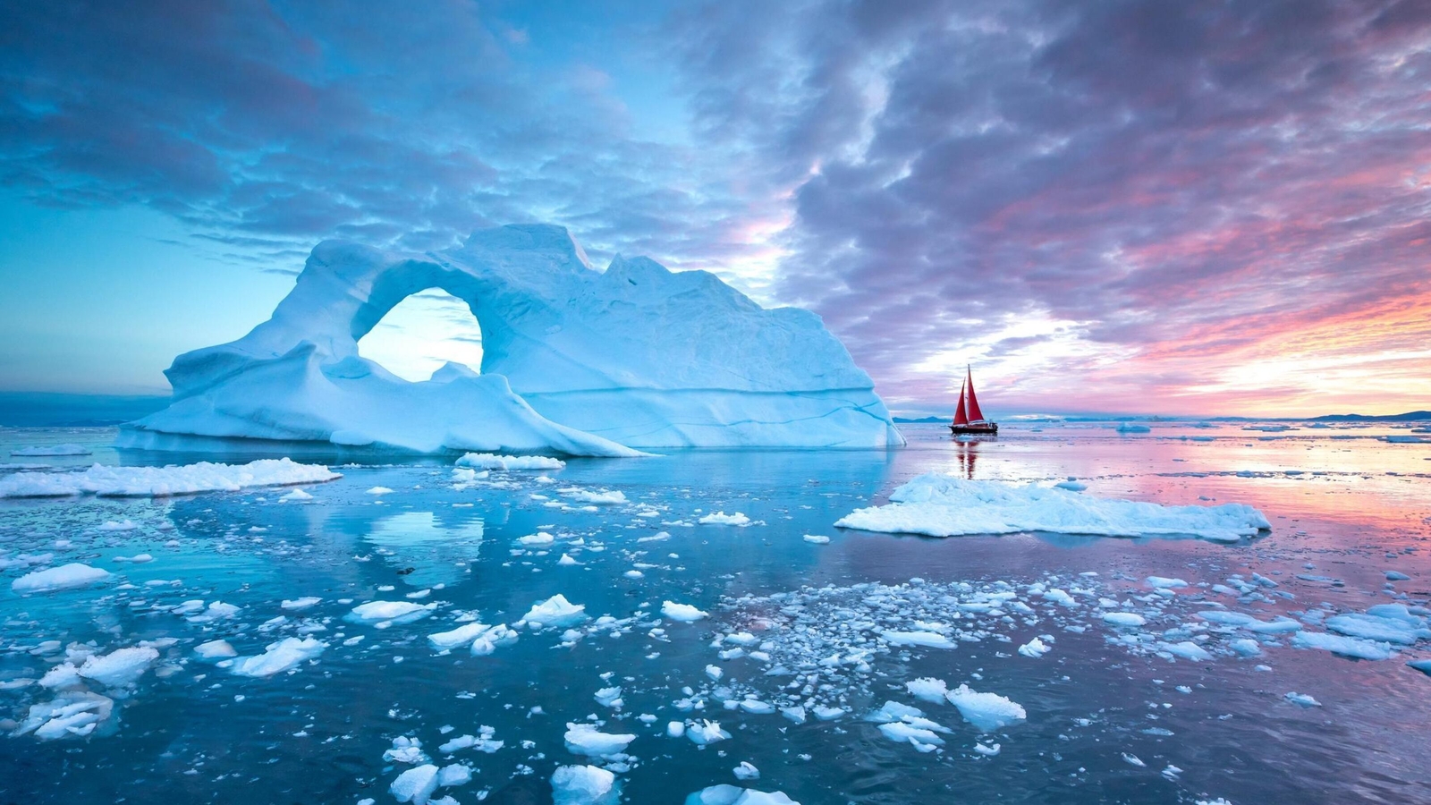 A small boat sailing next to an iceberg at sunset in Greenland