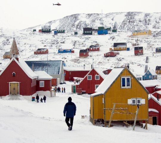 People walking among houses in the Inuit town of Ittoqqortoormiit in Greenland
