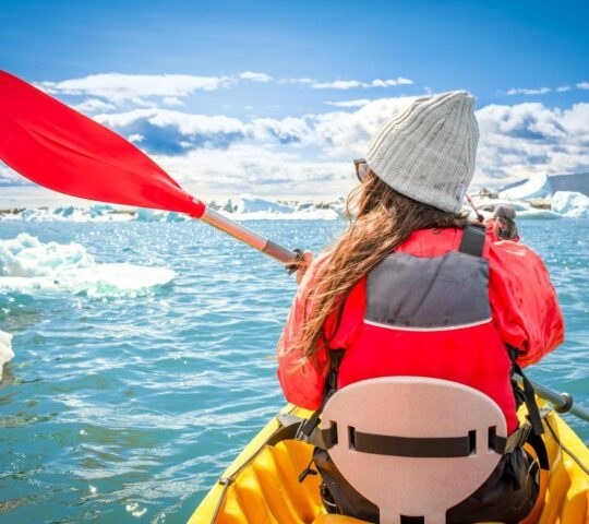 View of the back of a woman kayaking in the Arctic