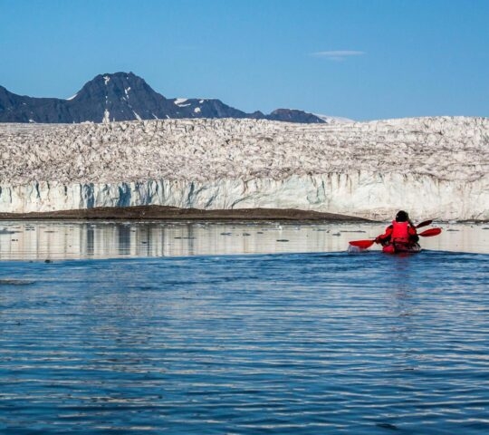 Two people in a kayak paddling in front of a glacier.