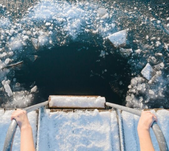 view of a woman's hands holding onto a handrail overlooking icy waters ready for swiming