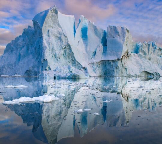 An iceberg reflected in still water at sunset