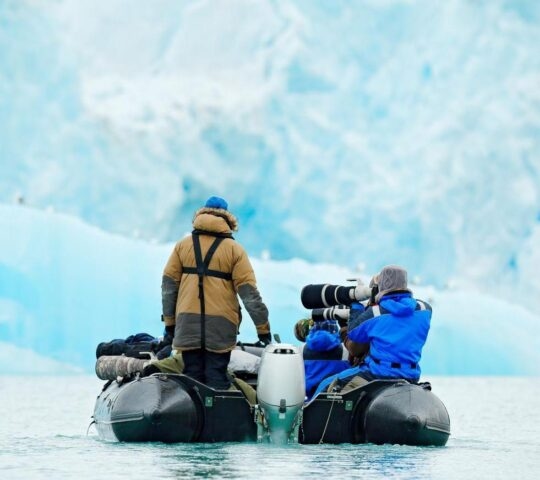 Two people in a zodiac boat with a large camera photographing Arctic scenery