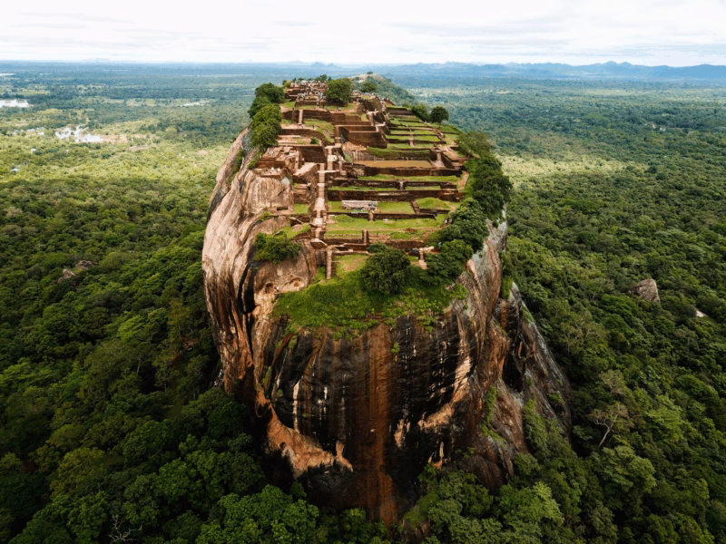 The ancient Sigiriya Rock fortress, a UNESCO World Heritage site in Sri Lanka, towering over lush tropical jungles under a clear sky.