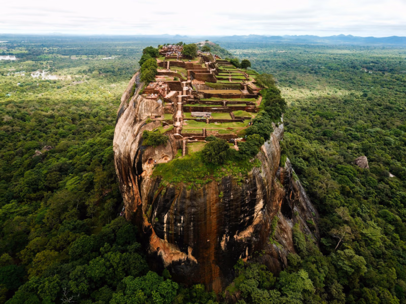 The ancient Sigiriya Rock fortress, a UNESCO World Heritage site in Sri Lanka, towering over lush tropical jungles under a clear sky.