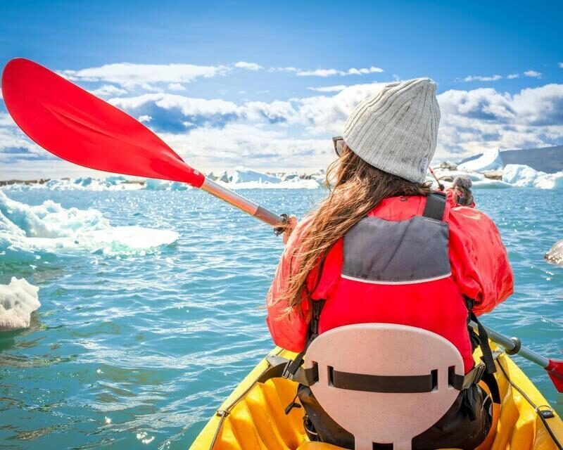 Woman in a kayak with a red paddle through antarctic or Icelandic glaciers.
