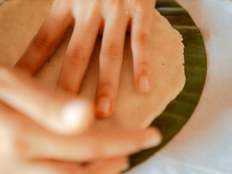 A close-up of hands flattening dough onto a circular green leaf during luxury Family vacations.