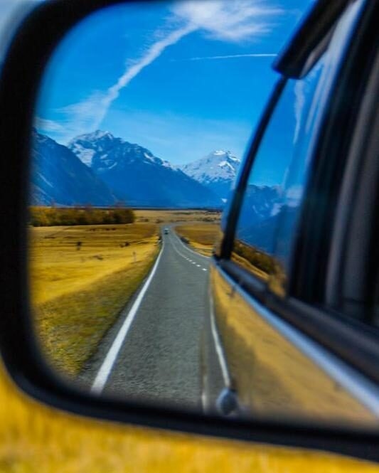 Roadtrip/car traveling concept. View of back car mirror with mountain and road scenery. Aoraki/Mount Cook National Park, South Island of New Zealand.