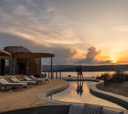 A couple stand by a pool at Wilderness Magashi Peninsula a luxury lodge in Rwanda.