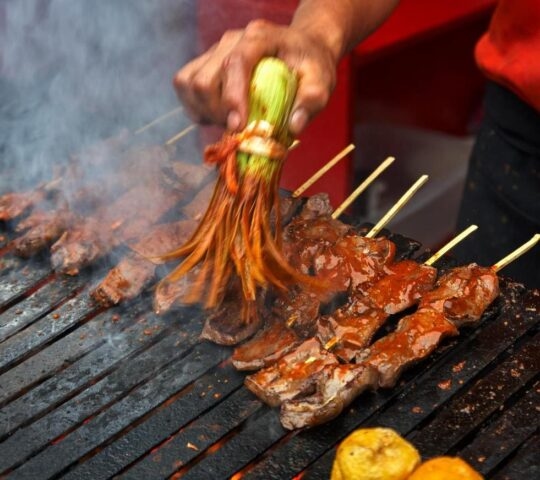 A man brushes sauce onto skewers of grilled anticuchos in Peru