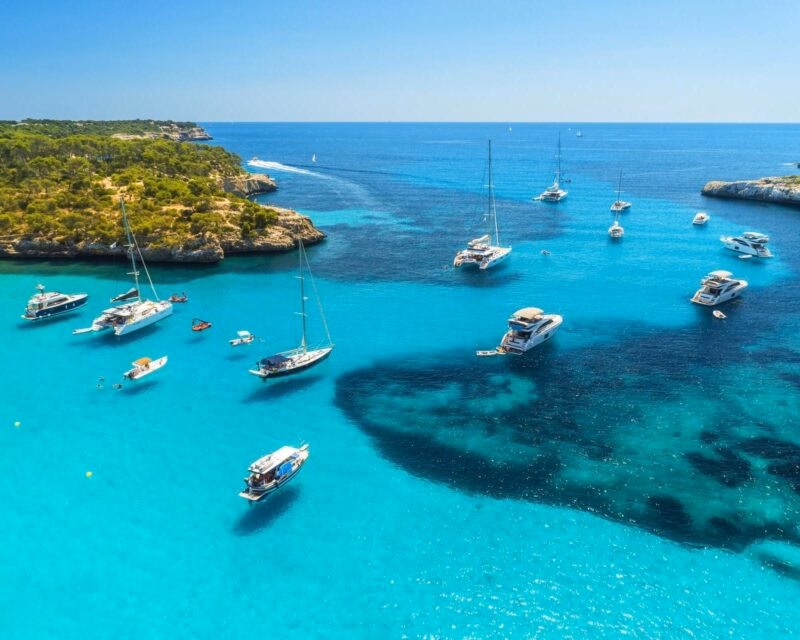 Aerial view of boats floating on bright turquoise water in a bay in Mallorca