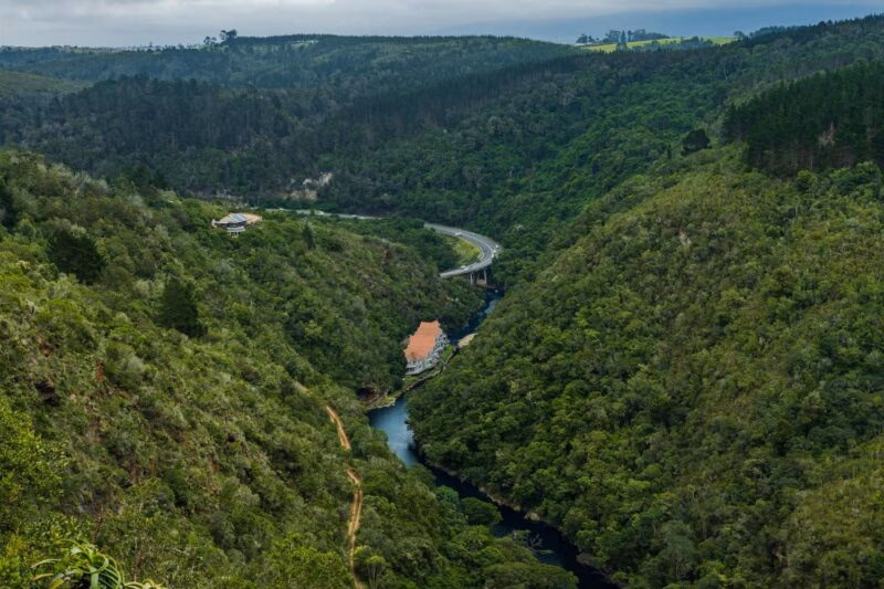 A river flows through a steep valley covered in thick green forest with a white building nestled on the bank.