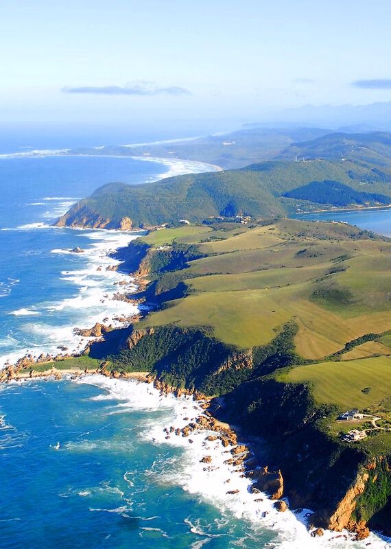 High-angle aerial view of a winding coastline with green cliffs meeting the deep blue ocean and white foam.