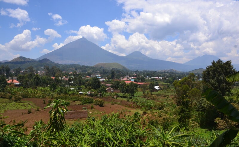 A distant view of the conical Mount Muhabura volcano rising above a green valley and a small village.