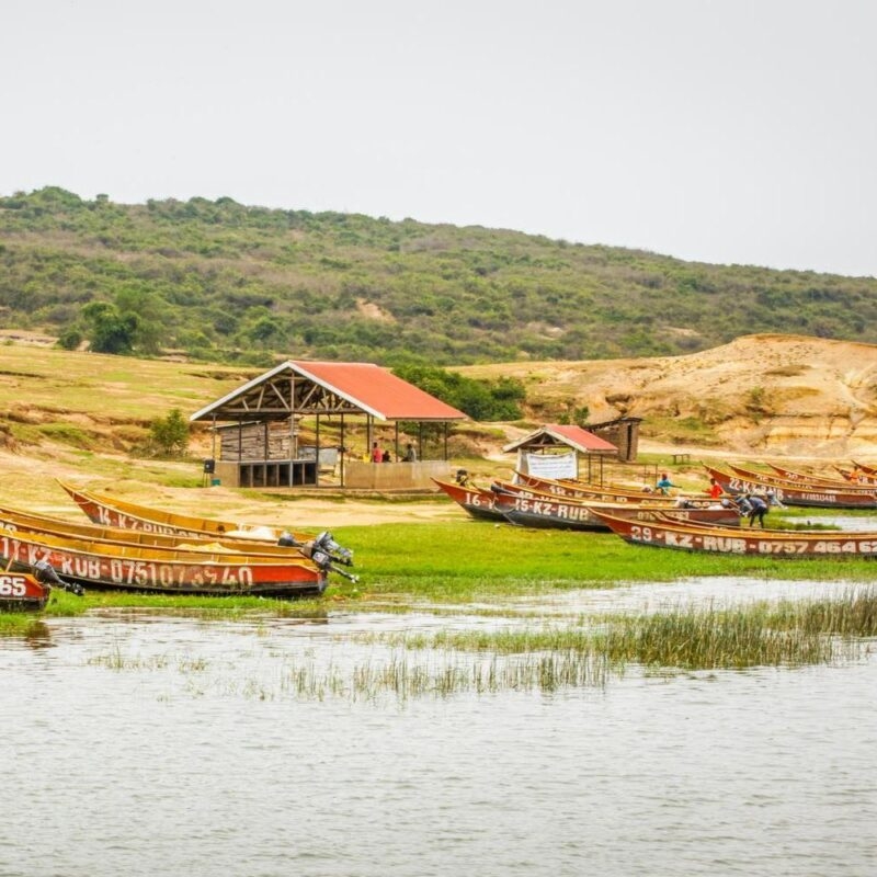 Row of narrow wooden boats on a riverbank near a small open-sided building with a red roof.