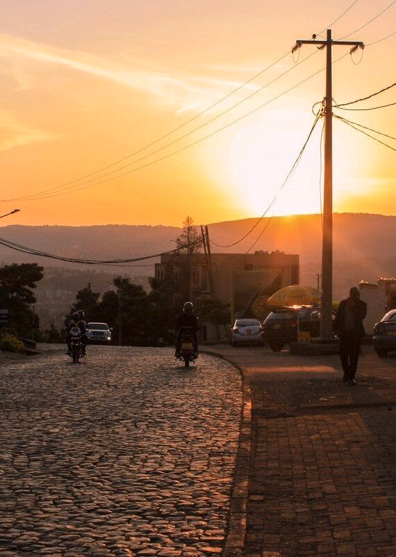 Silhouetted commuters on a cobblestone street in Kigali during a golden sunset with a utility pole.