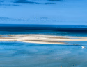 Aerial view of a white sandbar and a small white boat in the turquoise waters of the Bazaruto Archipelago.