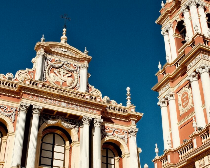 Ornate pink and white colonial church with a tall bell tower and classical columns under a clear blue sky in Salta.