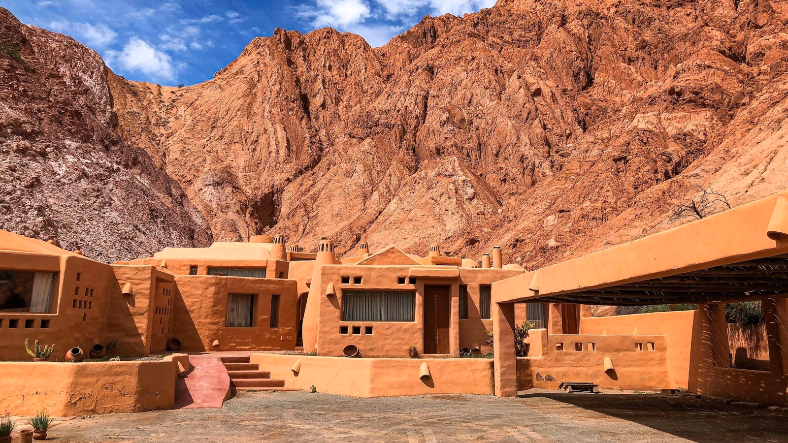 Modern adobe buildings with a reddish-orange finish nestled against a steep, rocky mountain face in Purmamarca.