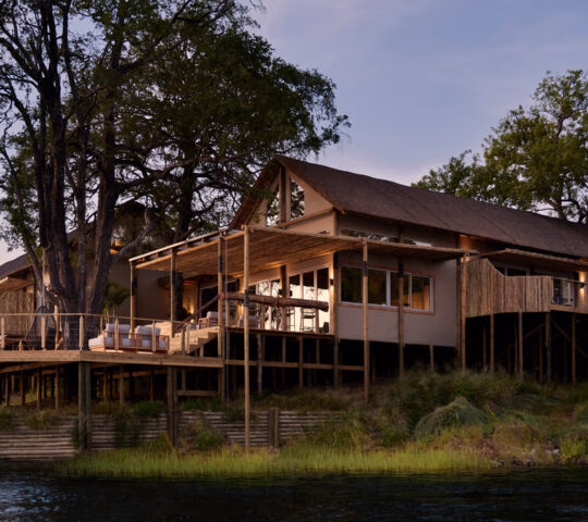 A large stilted luxury villa at Victoria Falls River Lodge with expansive wooden decks situated along the riverbank.