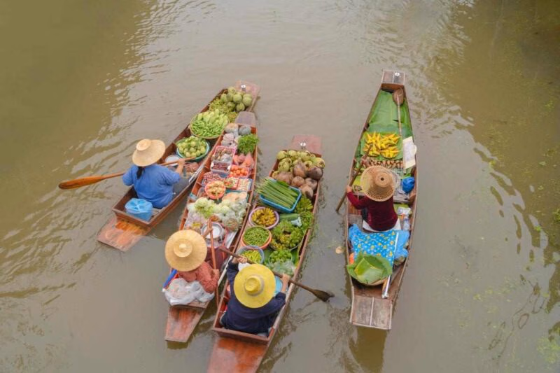 Overhead view of vendors in wooden boats filled with colourful produce on a Bangkok canal.