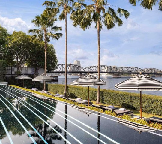 Black tiled infinity pool with white stripes overlooking a river and bridge at the Siam in Bangkok.