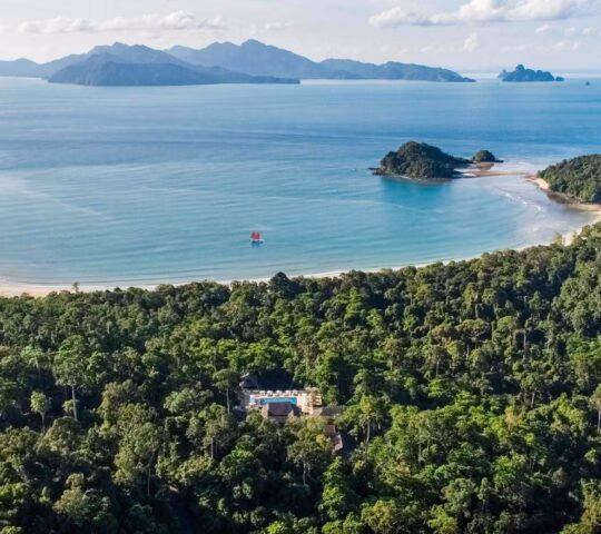 Aerial shot of the Datai in the jungle overlooking a wide bay with a sailboat.
