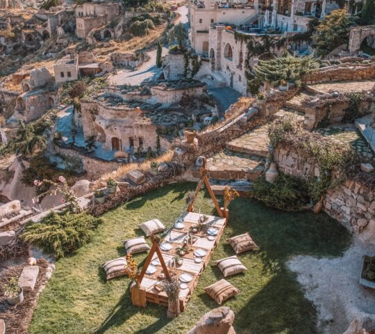 Low dining table with pillows on a green terrace overlooking the stone cave architecture of Argos in Cappadocia.