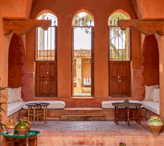A terracotta-walled courtyard with three arched windows, low cushioned seating, and decorative pottery at Al Moudira Luxor.