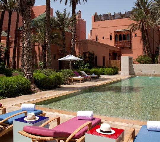 A long outdoor swimming pool with pink and blue loungers at the luxury Royal Mansour resort in Marrakech.