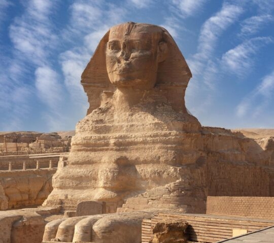 Front view of the Great Sphinx of Giza in Egypt with desert landscapes and a blue sky in the background.