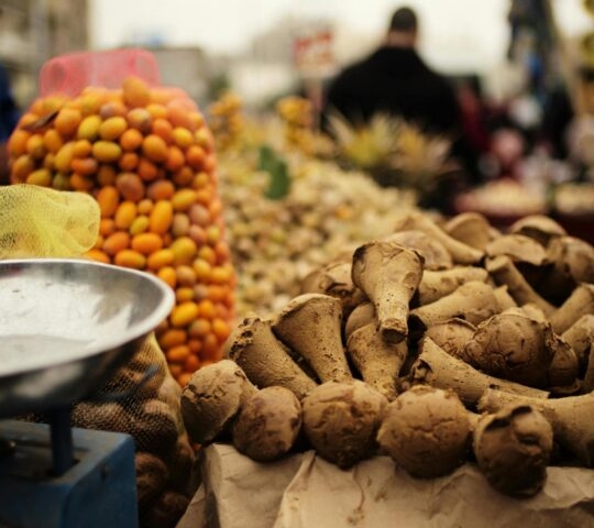 A close-up of a Cairo night food market tour showing bags of orange fruit and brown cone-shaped goods next to a scale.