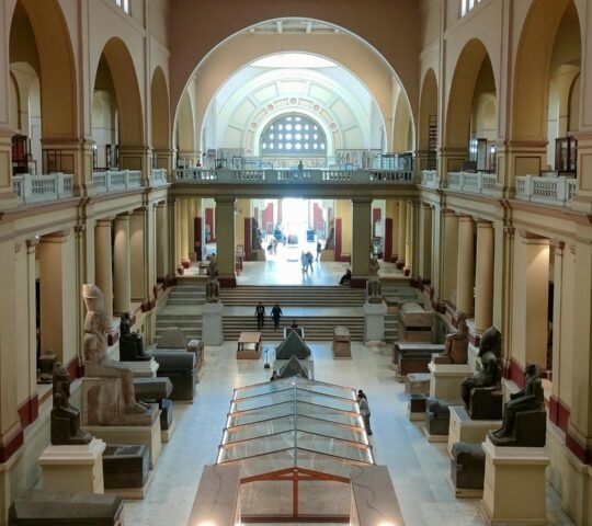 Wide view of the interior hall of the National Museum of Egyptian Civilization featuring ancient statues and stone sarcophagi.