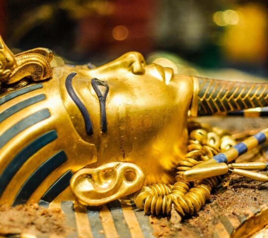Side profile of the golden burial mask of Tutankhamun with blue stripes and a ceremonial beard.