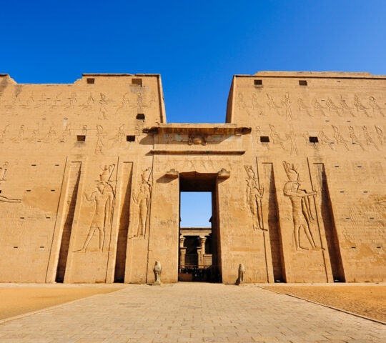 Large sandstone pylon of the Temple of Edfu with ancient Egyptian carvings and a central doorway.