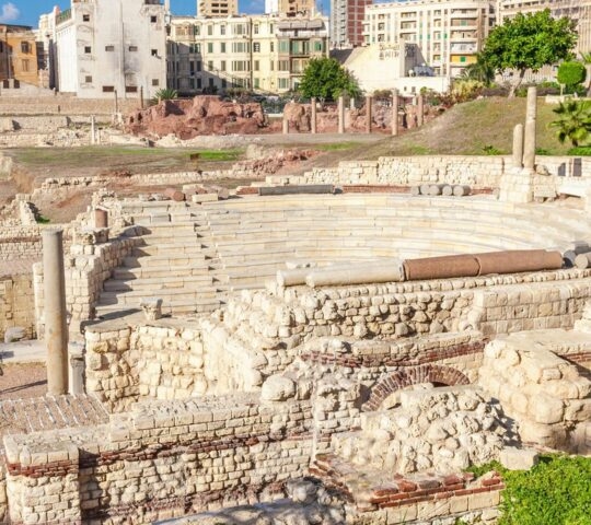 Elevated view of an ancient Roman amphitheater with stone tiers and ruins in Alexandria, Egypt.