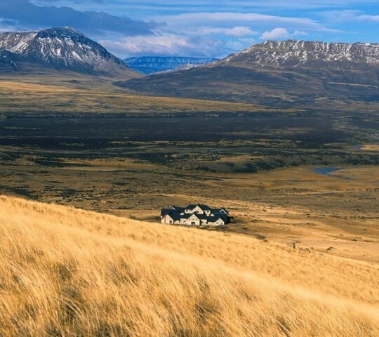 Wide view of Eolo lodge surrounded by grassy plains with mountains in the background in Patagonia