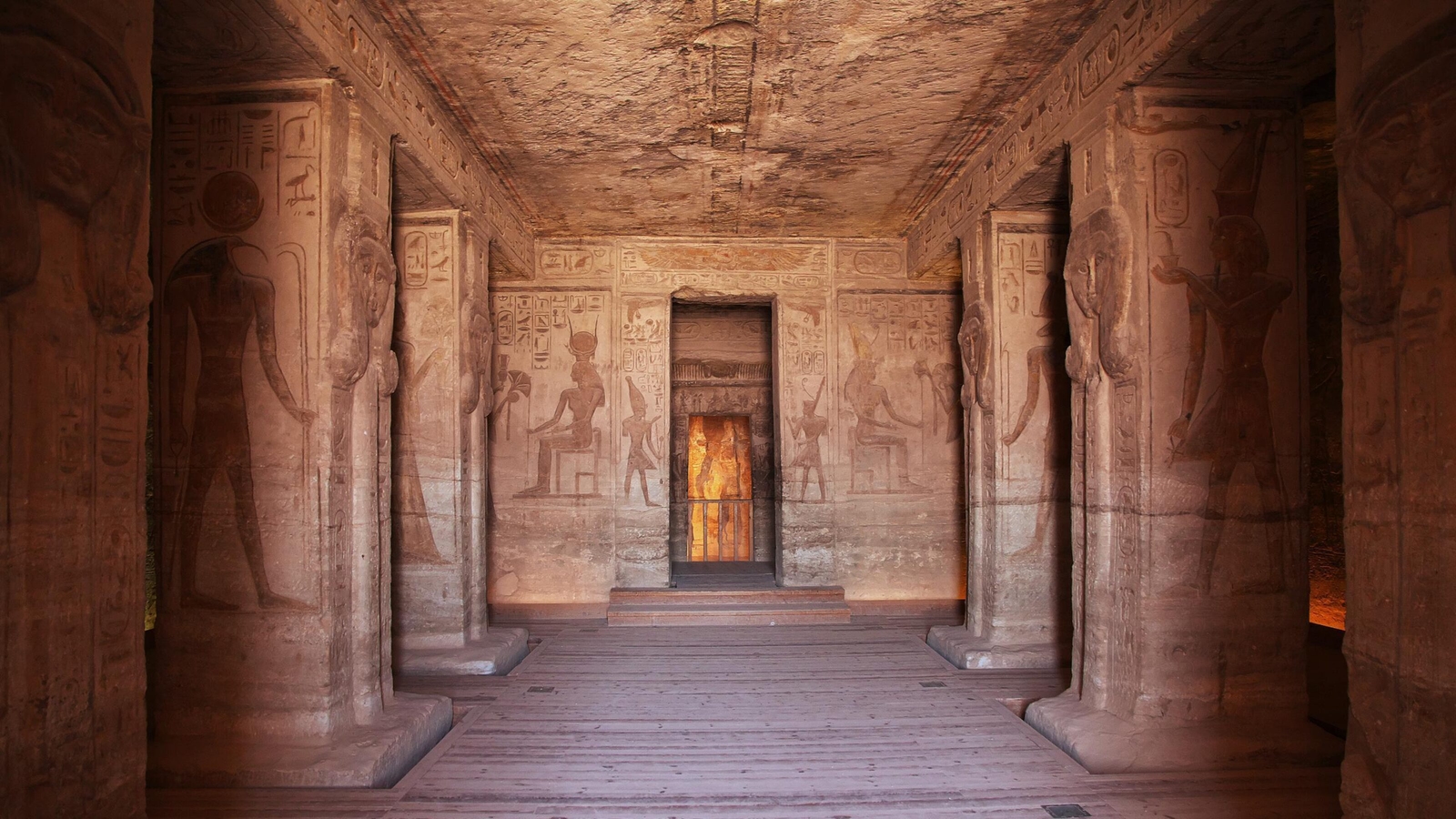 The interior of an ancient Egyptian temple featuring large stone pillars and walls covered in detailed carvings.
