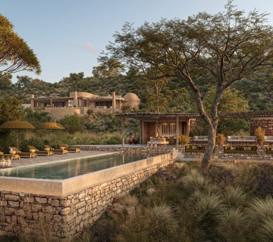 A rectangular stone infinity pool with yellow umbrellas and lounge chairs at Suyian Lodge, surrounded by trees and hills.