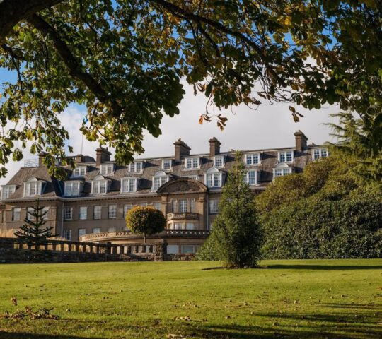 The exterior of Gleneagles hotel in Scotland, half covered by greenery and with a large tree in the foreground