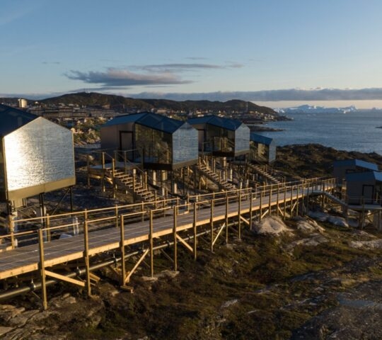 Glass and wood huts on a rocky shore reflecting the sea at Hotel Arctic in Greenland
