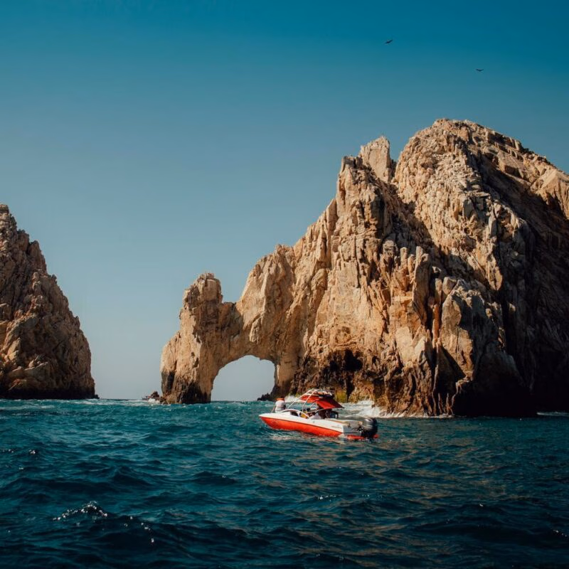 A red boat sails near the El Arco rock formation in Cabo San Lucas, Mexico.