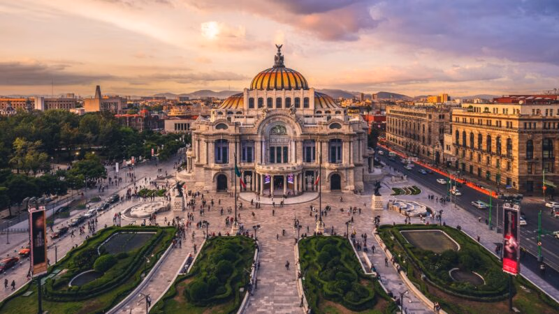 The Palacio de Bellas Artes in Mexico City at sunset with surrounding gardens.