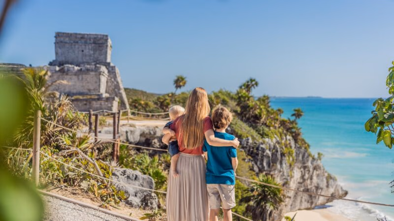 Family stands at Tulum ruins overlooking the ocean during a Mexico family vacation.
