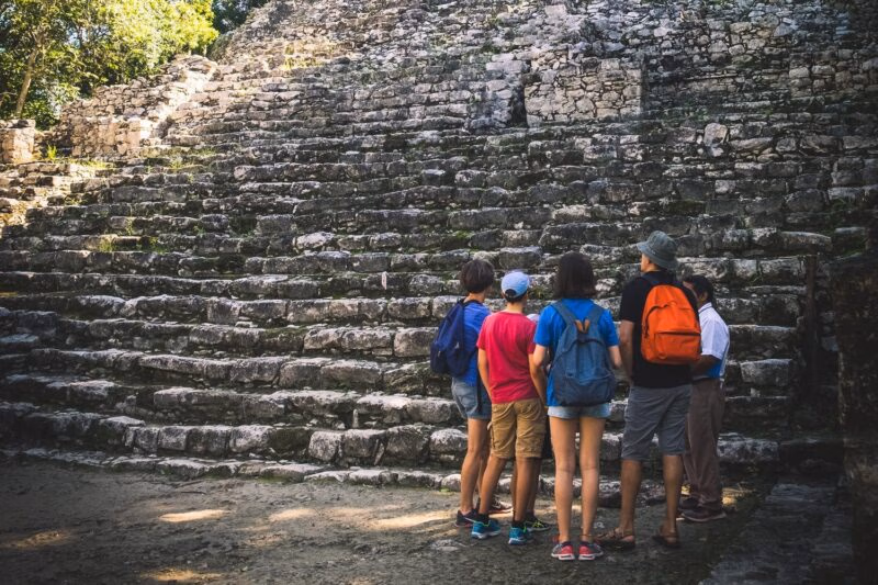A group of travelers stands before ancient stone ruins while on a Mexico family vacation.