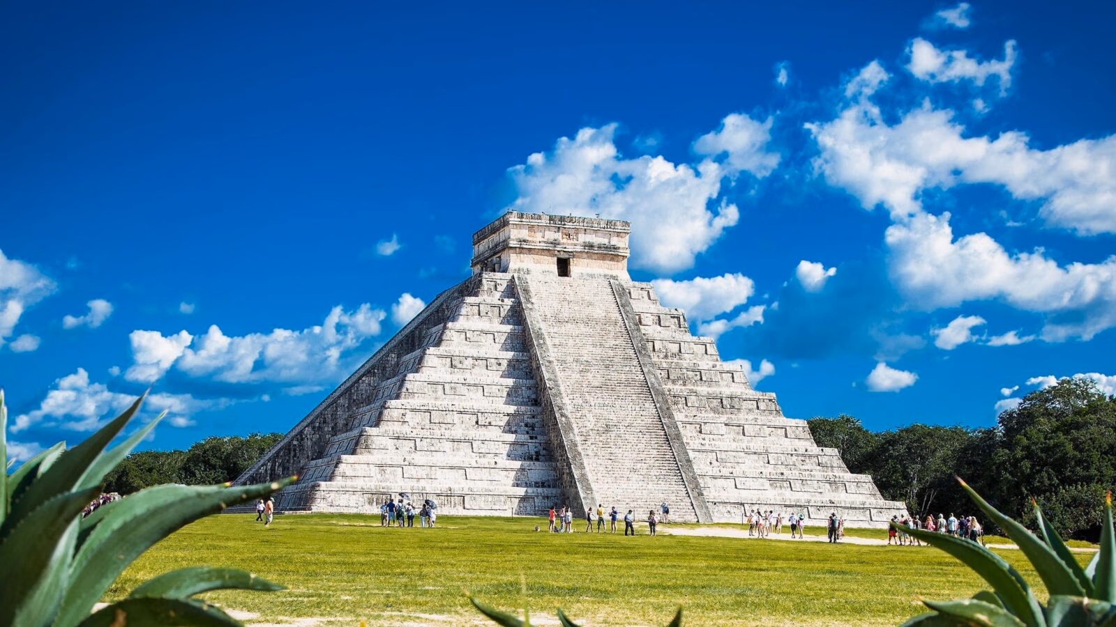 The ancient Mayan pyramid of Chichen Itza in Mexico surrounded by green grass and visitors.