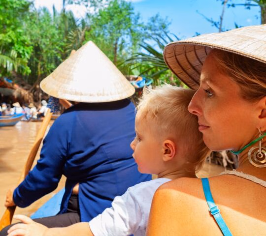 A woman and young boy on a boat ride through a lush Vietnamese waterway with a rower in a conical hat.